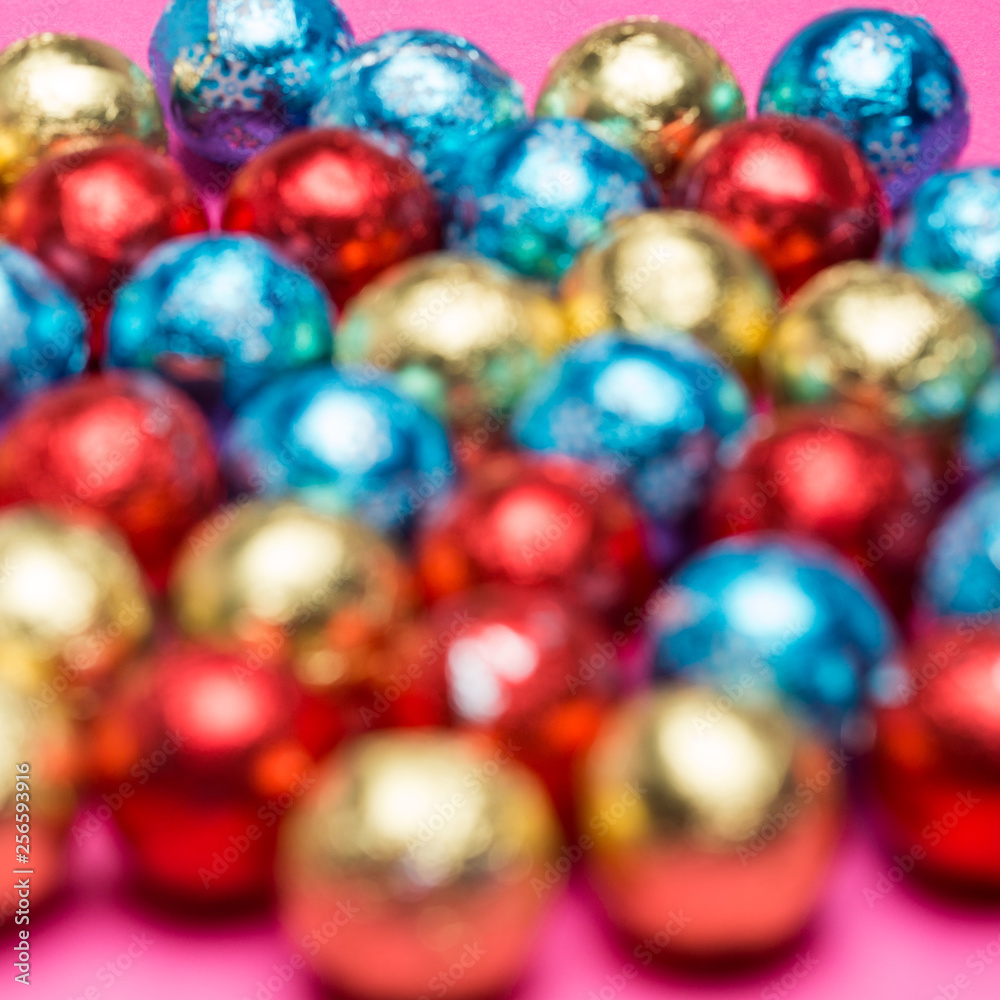 Blurry round chocolate candies in a multi-colored foil on a pink background Blurry round chocolate candies in a multi-colored foil on a pink background