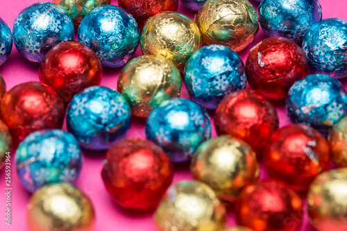 Blurry round chocolate candies in a multi-colored foil on a pink background