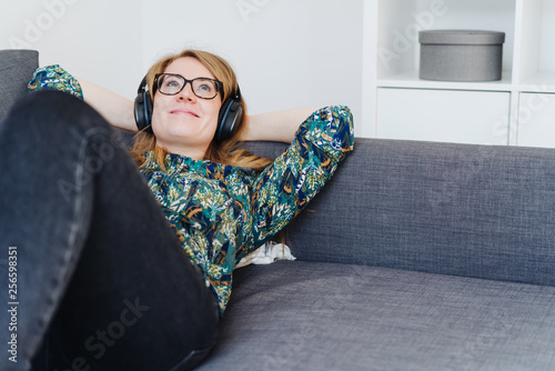 Happy young woman listening to music on a sofa