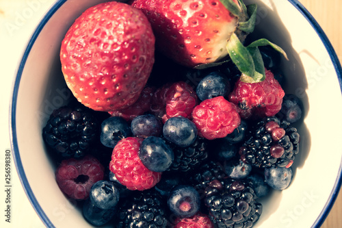Bowl of fresh berries: strawberries, blueberries, raspberries and blackberries; natural morning light, wooden background. Healthy eating