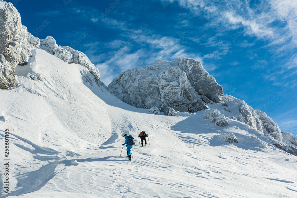 Hikers approach the snowy slope under icy rocks.