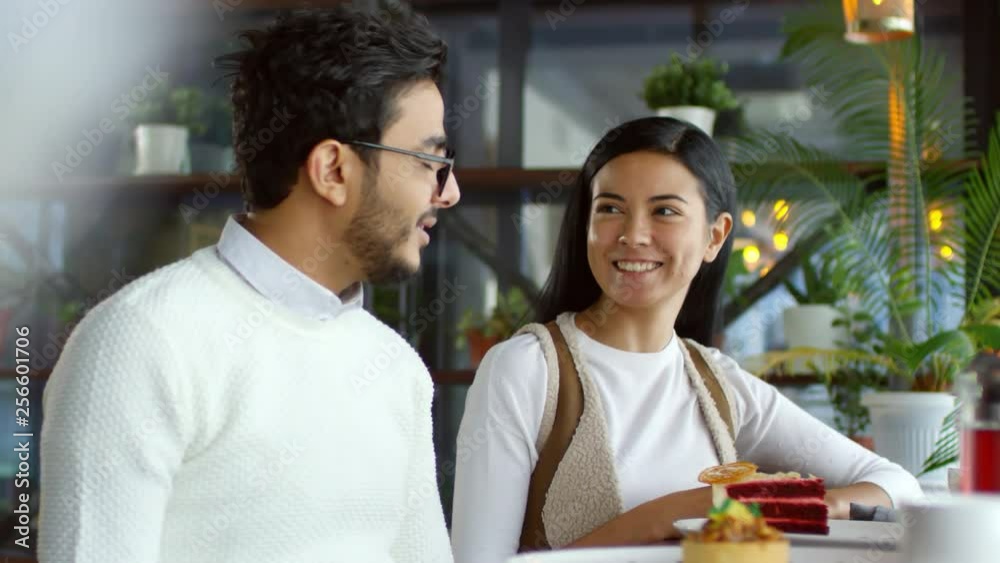 Young beautiful Asian woman and middle eastern man sitting at cafe table with desserts, smiling and speaking Young beautiful Asian woman and middle eastern man sitting at cafe table with desserts, smiling and speaking