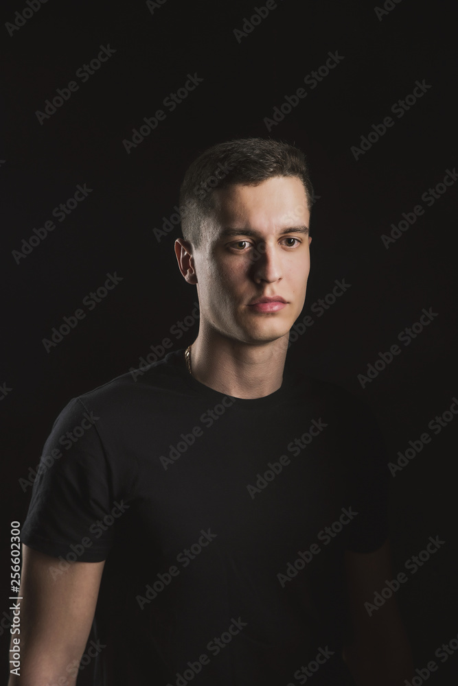 Beautiful, slender young man in black t-shirt on black background and on the street
