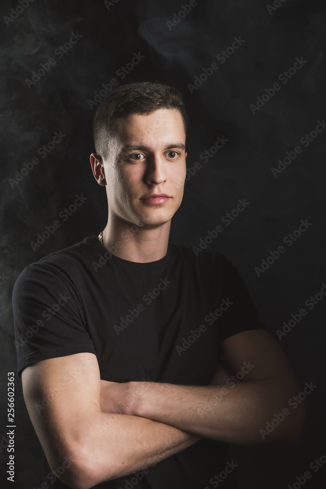 Beautiful, slender young man in black t-shirt on black background and on the street