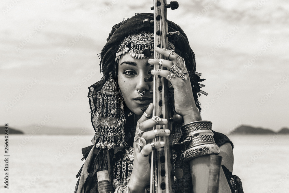 Fototapeta Beautiful young stylish tribal woman in oriental costume playing sitar outdoors. Close up