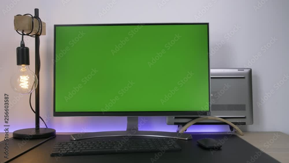 Modern monitor with green screen display standing in a desk of an office with a laptop and a lamp bulb. Modern monitor with green screen display standing in a desk of an office with a laptop and a lamp bulb.