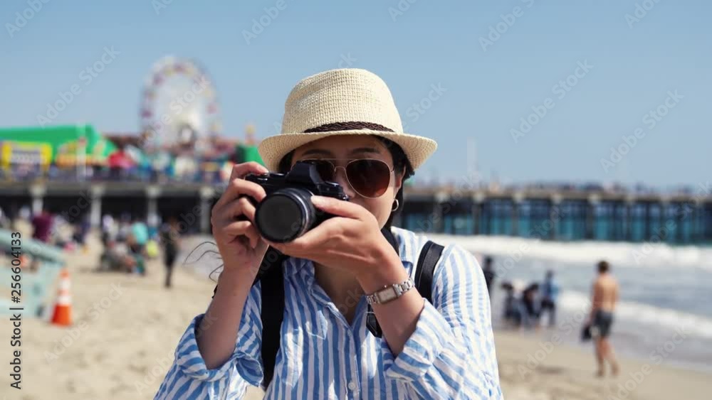 happy asian female photographer holding slr camera taking photo picture of nature sandy beach bay summer view Santa Monica Pier. people relaxing having fun in background with water sea and waves. happy asian female photographer holding slr camera taking photo picture of nature sandy beach bay summer view Santa Monica Pier. people relaxing having fun in background with water sea and waves.