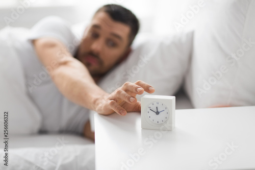 Fotografia morning and people concept - close up of sleepy young man in bed reaching for al