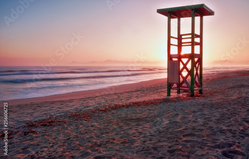 Lifeguard tower, sunrise, footprints on secluded beach with mountains and calm sea, playa de muro, alcudia, mallorca, spain.