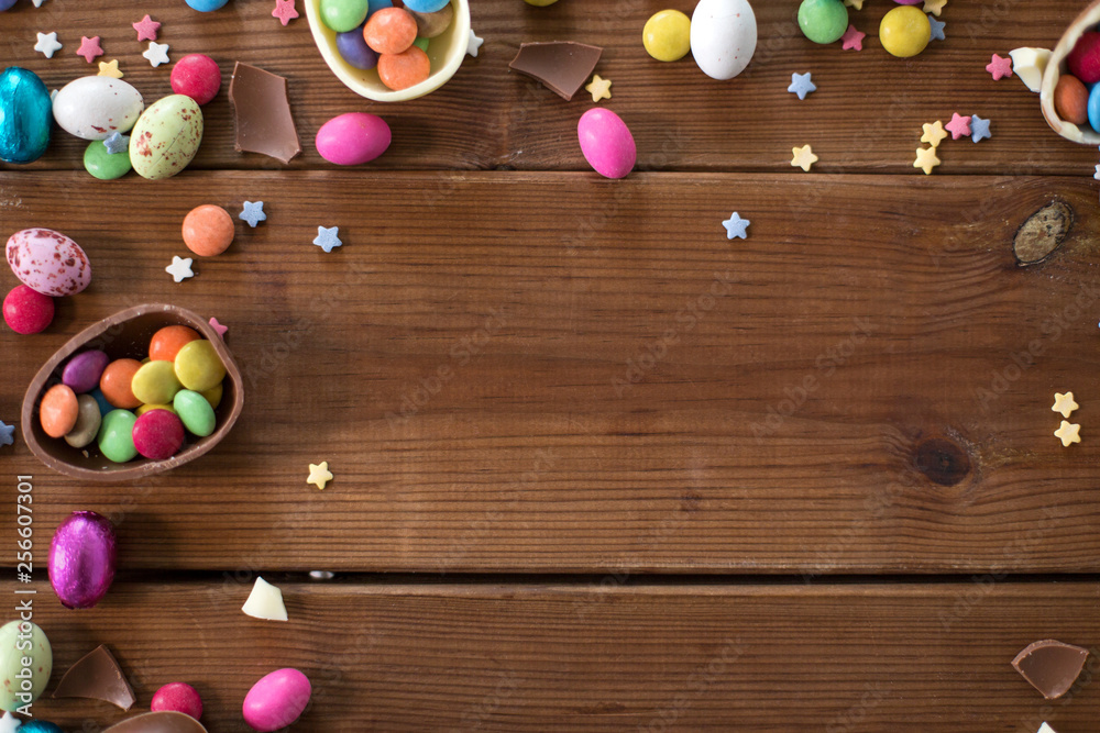 Obraz premium easter, sweets and confectionery concept - chocolate eggs and candy drops on wooden background
