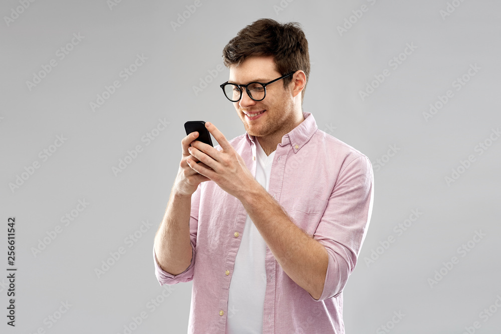 technology, internet and people concept - smiling young man in glasses looking at smartphone over grey background technology, internet and people concept - smiling young man in glasses looking at smartphone over grey background