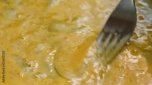 Close slow motion video of scrambling eggs in a skillet with a fork illuminated with natural lighting.