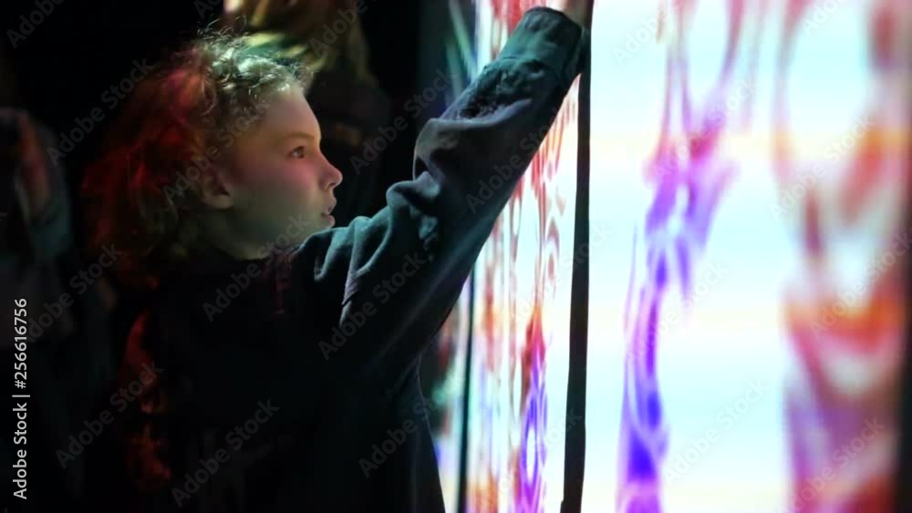 Boy touches a hand to a huge interactive wall. Large glowing screen with glowing patterns