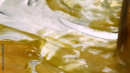 Close slow motion video of stirring two eggs in a skillet for scrambling with a wood spoon illuminated with natural lighting.
