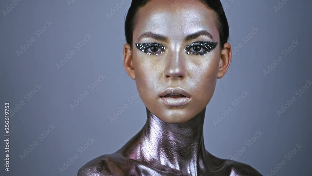 Fashion model young woman in trendy glowing skin make-up posing in studio. Eye models with glitter on the eyelids. Neck and chest are covered with metallic make-up