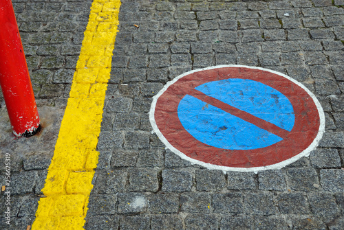 Forbidden parking sign painted on paving stones, close to yellow line and red pylon. © trialartinf