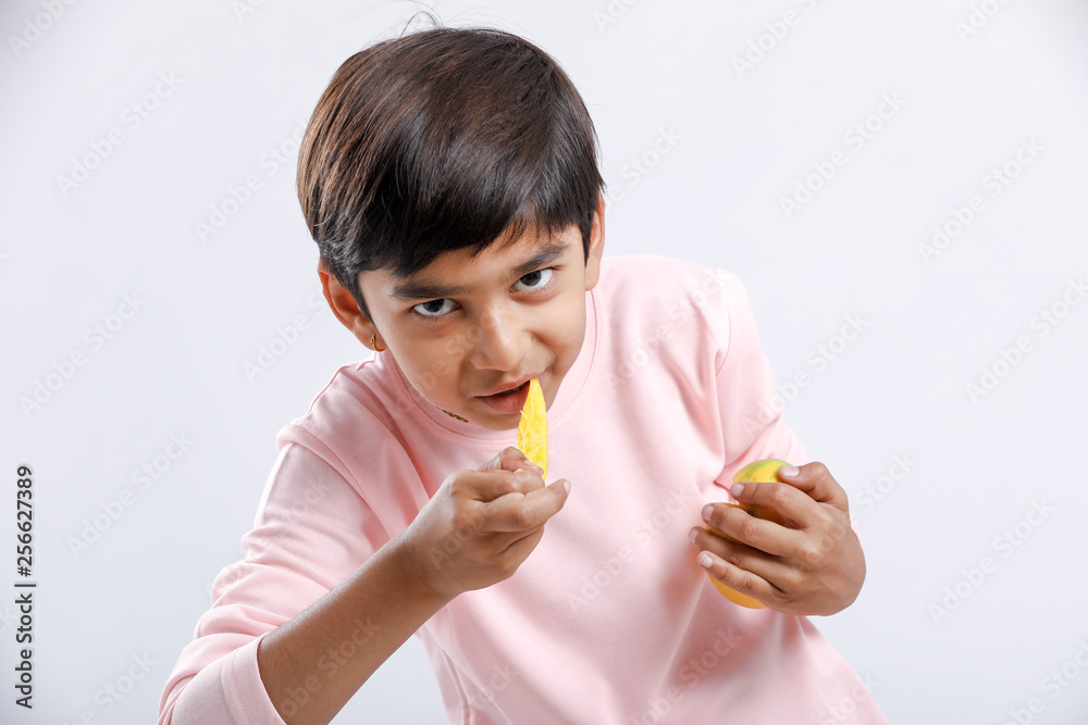 Cute indian/Asian little boy eating Mango with multiple expressions. isolated over white background Cute indian/Asian little boy eating Mango with multiple expressions. isolated over white background