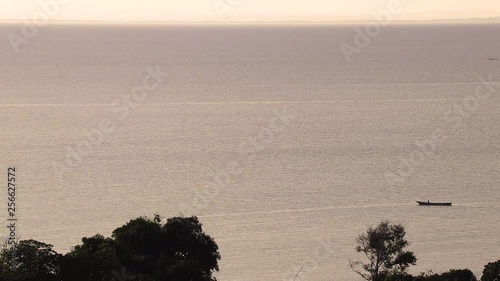 Lone fishing boat out on the water at dusk in Kalangala, Lake Victoria. Wide view from hill on island in Uganda. Other boat visible by distant horizon in evening sunlight. photo