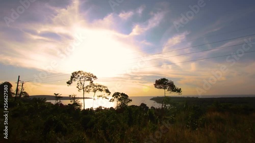 Bright evening sunlight shines through clouds and trees on island in Lake Victoria. Filmed from hill in Kalangala, Uganda. Dense forest, water and blue sky with scattered clouds visible. photo