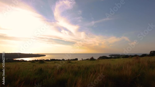 Islands in Lake Victoria seen from hill in Kalangala, Uganda. Forest, open water and blue sky with scattered clouds visible in evening sunlight. Tall grass sways in foreground. photo