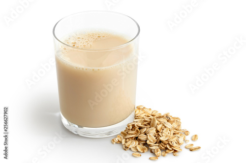 Glass of oat drink  next to a pile of dry oats isolated on white. photo