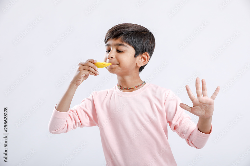 Cute indian/Asian little boy eating Mango with multiple expressions. isolated over white background