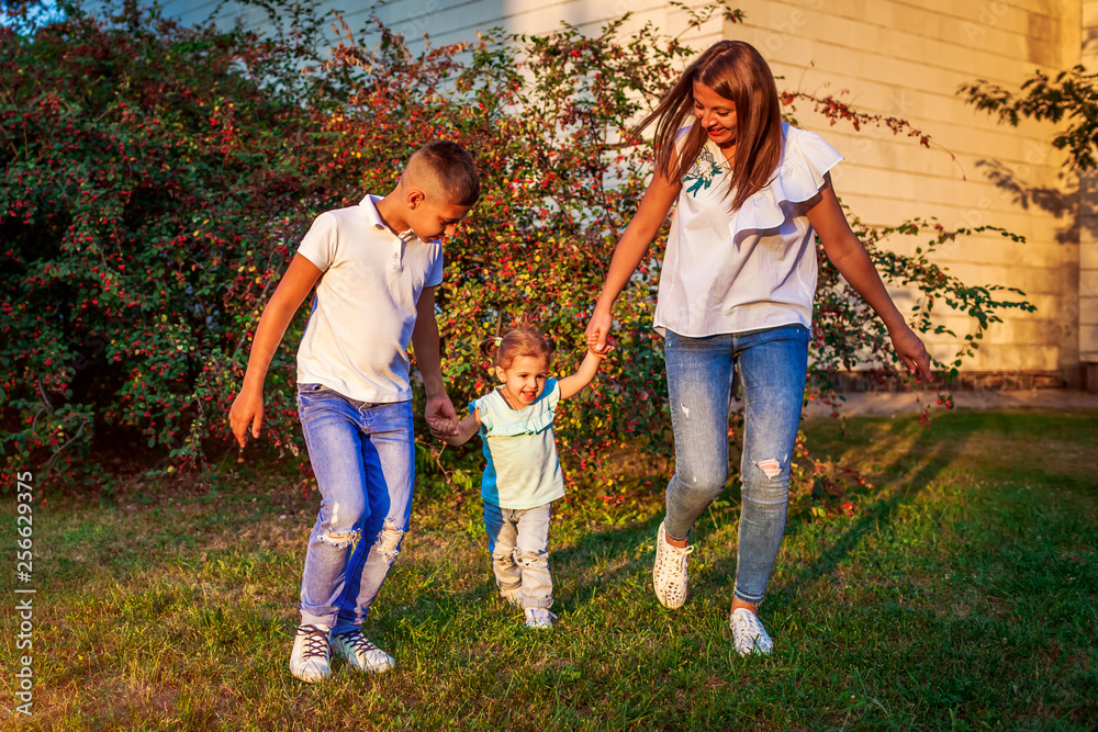 Fototapeta premium Happy family spending time outdoors walking in park. Mother and her son holding little toddler girl. Mother's day