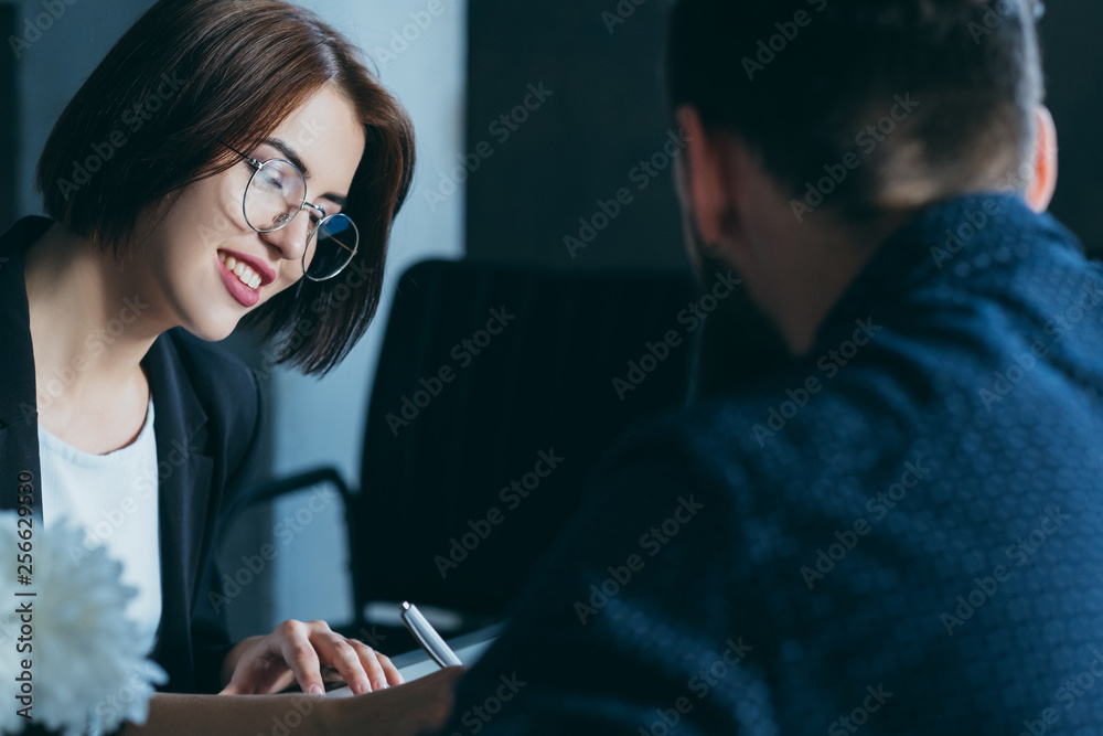 Coworking colleagues. Business matters discussion. Office workplace. Smiling female making notes. Coworking colleagues. Business matters discussion. Office workplace. Smiling female making notes.