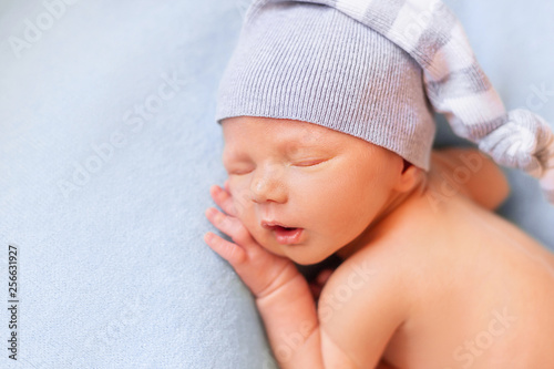 Sleeping newborn baby on the blue background. Child in a nightcap close-up portrait photo