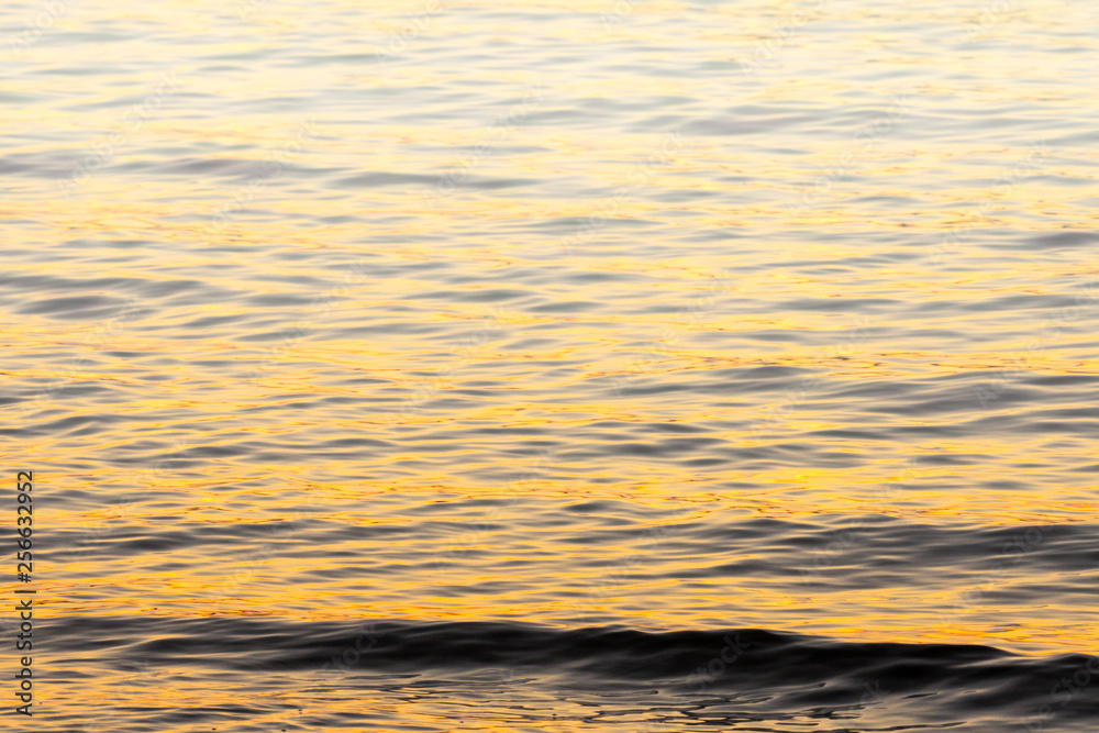 small wave and water ripple background in orange evening sunset light and fog rising in the distance