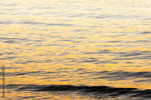 small wave and water ripple background in orange evening sunset light and fog rising in the distance