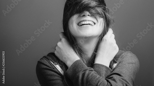 Cheerful mood. Young woman covering eyes with hair. Toothy smile. Black and white portrait. Copy space.