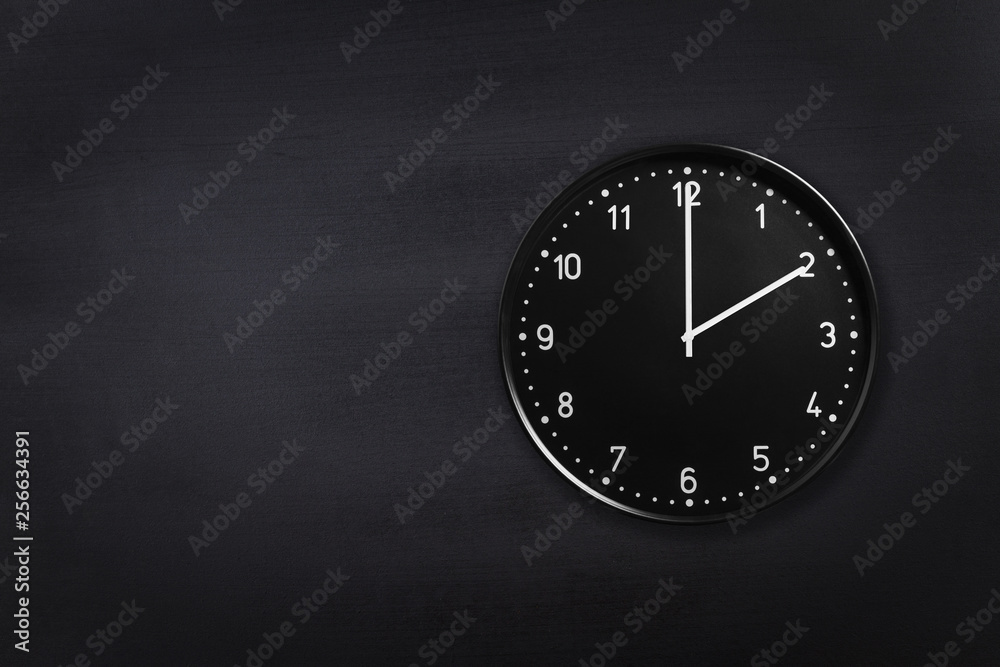 Black wall clock showing two o'clock on black chalkboard background