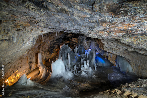 Underground glacier in Glaciers Cave in Apuseni mountains, Scarisoara, Romania. Ice and big icicles with colorful back light. Stalactites and stalagmites in dark cave photo