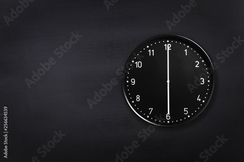 Black wall clock showing six o'clock on black chalkboard background. Office clock showing 6am or 6pm on black texture