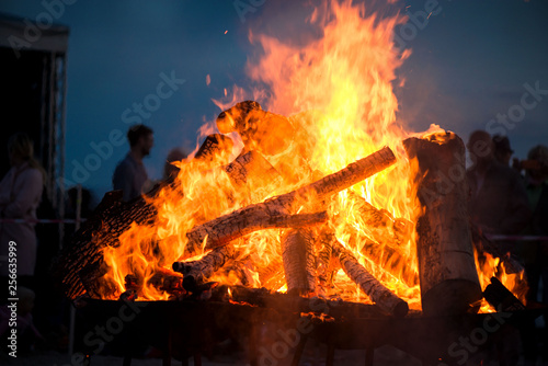 Large burning bonfire with soft glowing flame and sparkles flying all around. Romantic summer evening, people relaxing and enjoying calmness at the seaside during the Night of ancient lights. 