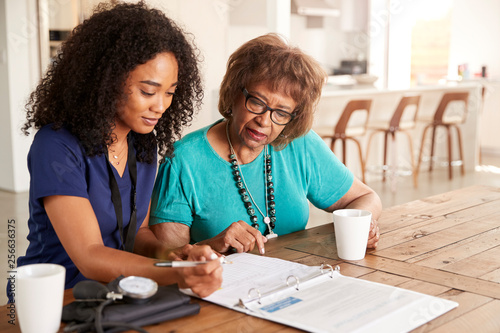 Female healthcare worker filling in a form with a senior woman during a home health visit photo
