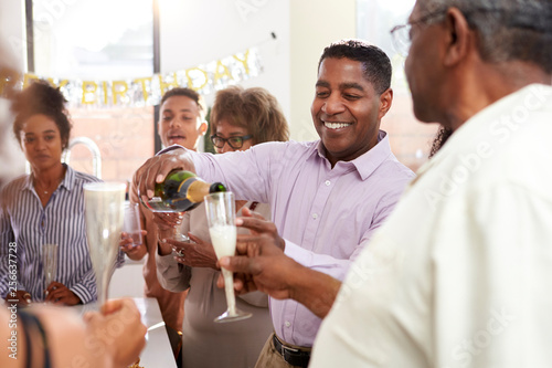 Middle aged black man pouring champagne to celebrate with his three generation family, close up