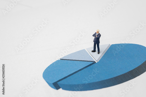 Miniature success and confidence businessman in suit standing on performance pie chart with black calculator using as work report, management profit and loss or company achievement and analysis
