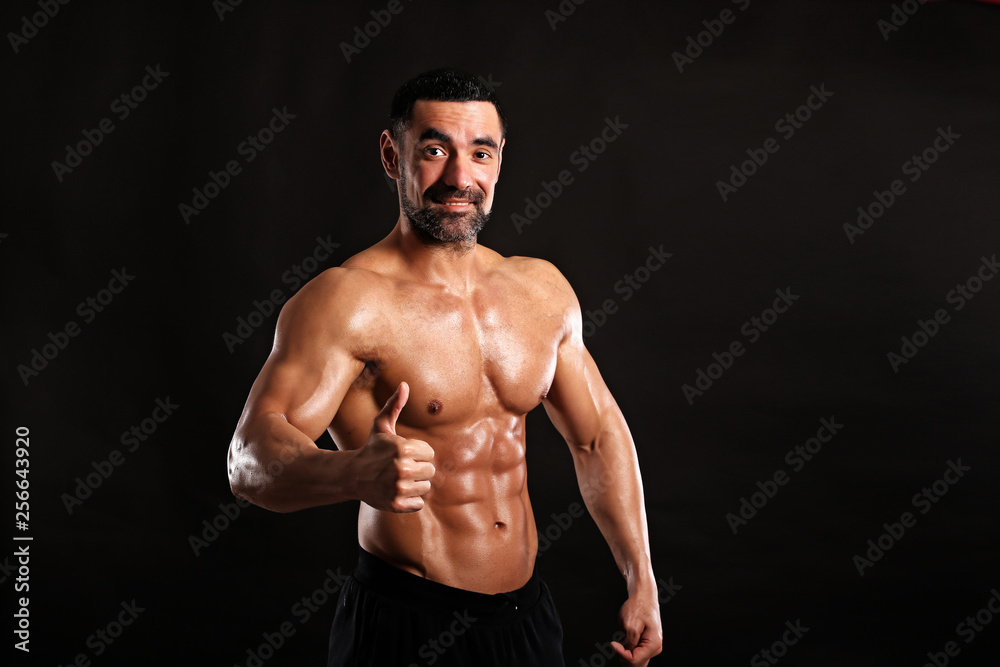 Portrait of young handsome  muscular bodybuilder on black background  showing big finger up , like 
