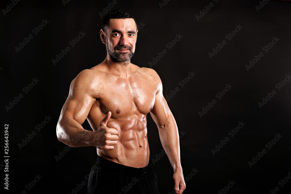 Portrait of young handsome  muscular bodybuilder on black background  showing big finger up , like 