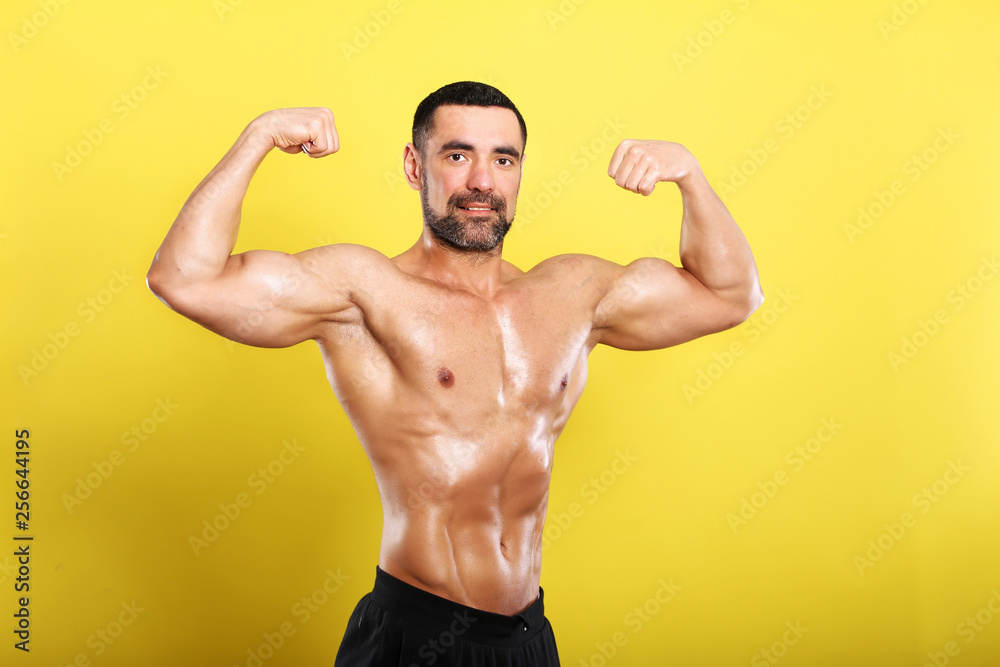 Portrait of young handsome  muscular bodybuilder on yellow background  with hands on 