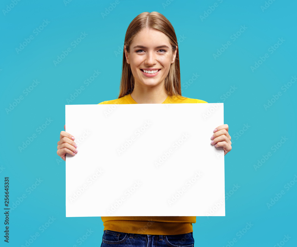 Smiling girl with white empty poster on blue background. Copy space for your text. Smiling girl with white empty poster on blue background. Copy space for your text.