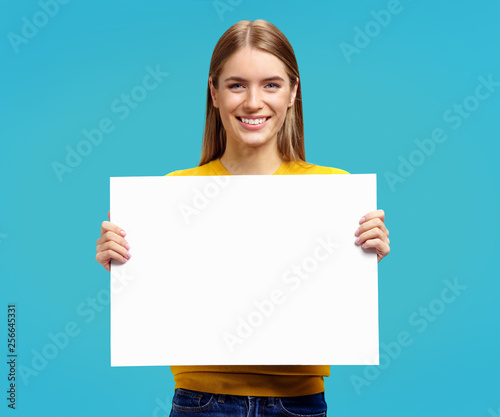Smiling girl with white empty poster on blue background. Copy space for your text.