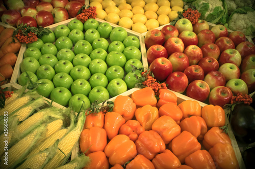 A counter on which green and red apples  lemons  bell peppers  carrots  corn  cauliflower and eggplants are neatly laid out