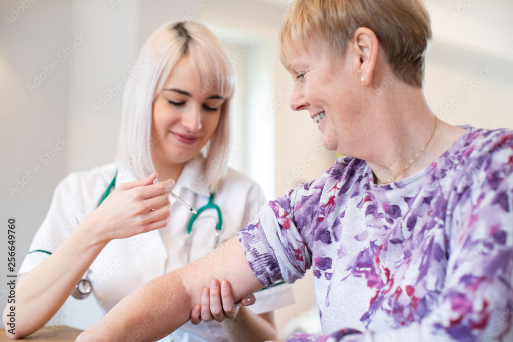 Female Nurse Giving Senior Woman Injection In Arm With Syringe Female Nurse Giving Senior Woman Injection In Arm With Syringe