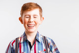 Portrait of a smiling red-haired boy with freckles and braces in a checkered shirt on a white background,