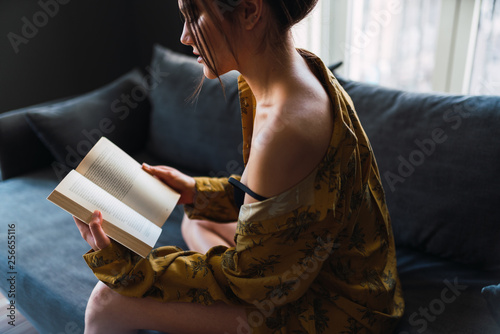 Obraz na płótnie Young woman with book sitting on sofa