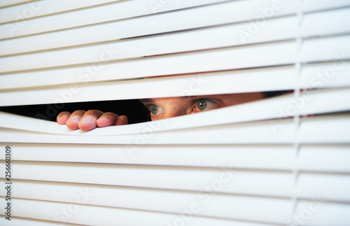A man looking through slats of blinds