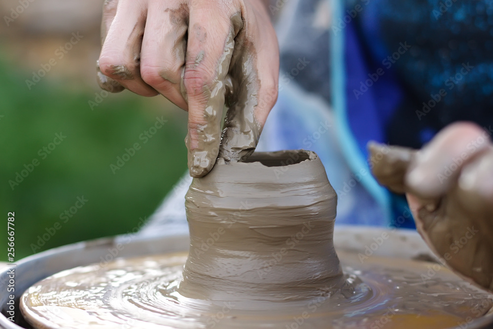 clay modeling, women's wet and dirty hands make a hole for the neck of a pot of clay on a Potter's wheel manual control at the master class on modeling